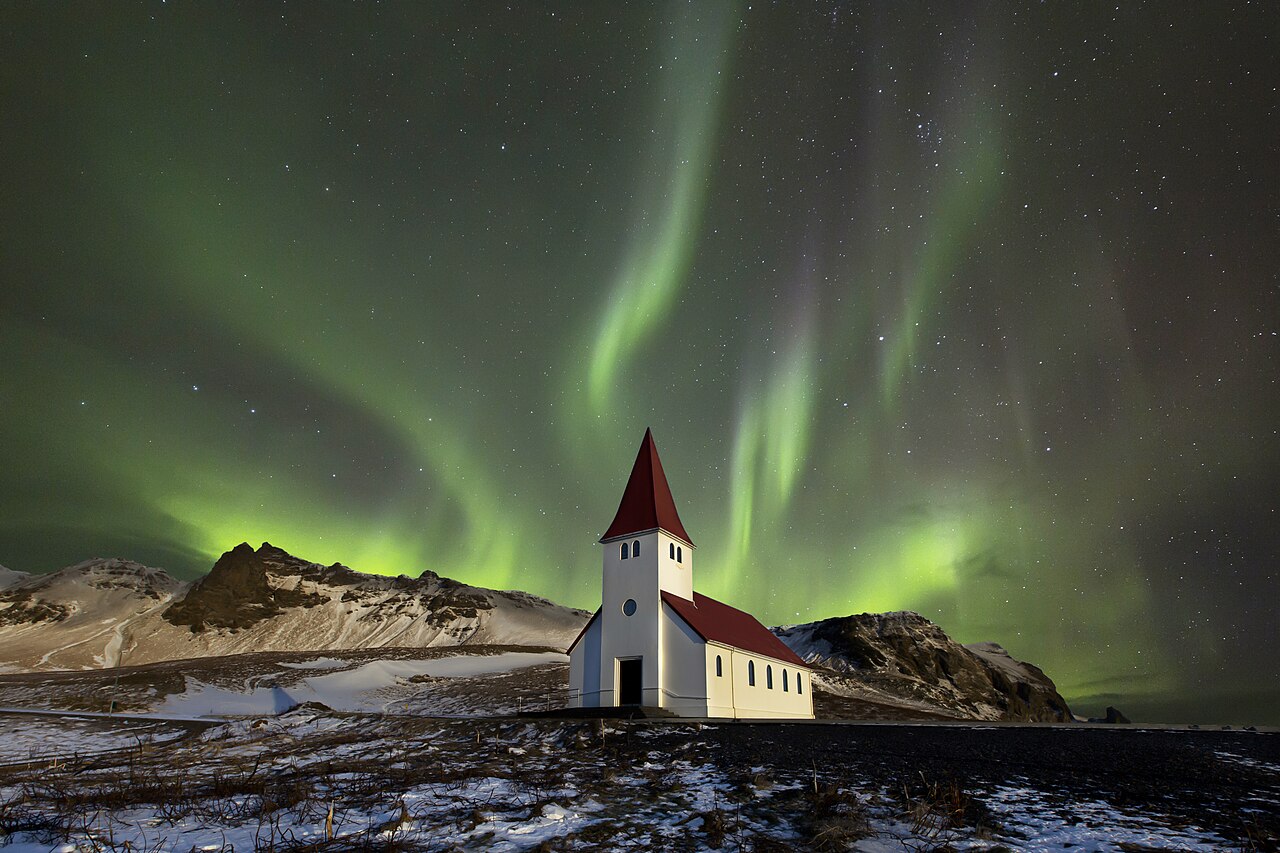 Northern lights dancing over a church in rural Iceland